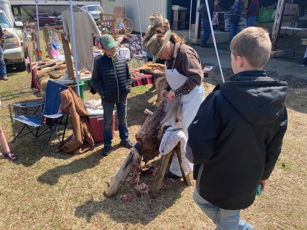 Shona Jordan, a taxidermist/hide tanner from Pike County, demonstrates to how to skin a hide to a couple of young attendees at the Arkansas Homesteading Conference Saturday at the Cleveland County Fairgrounds in Rison.
