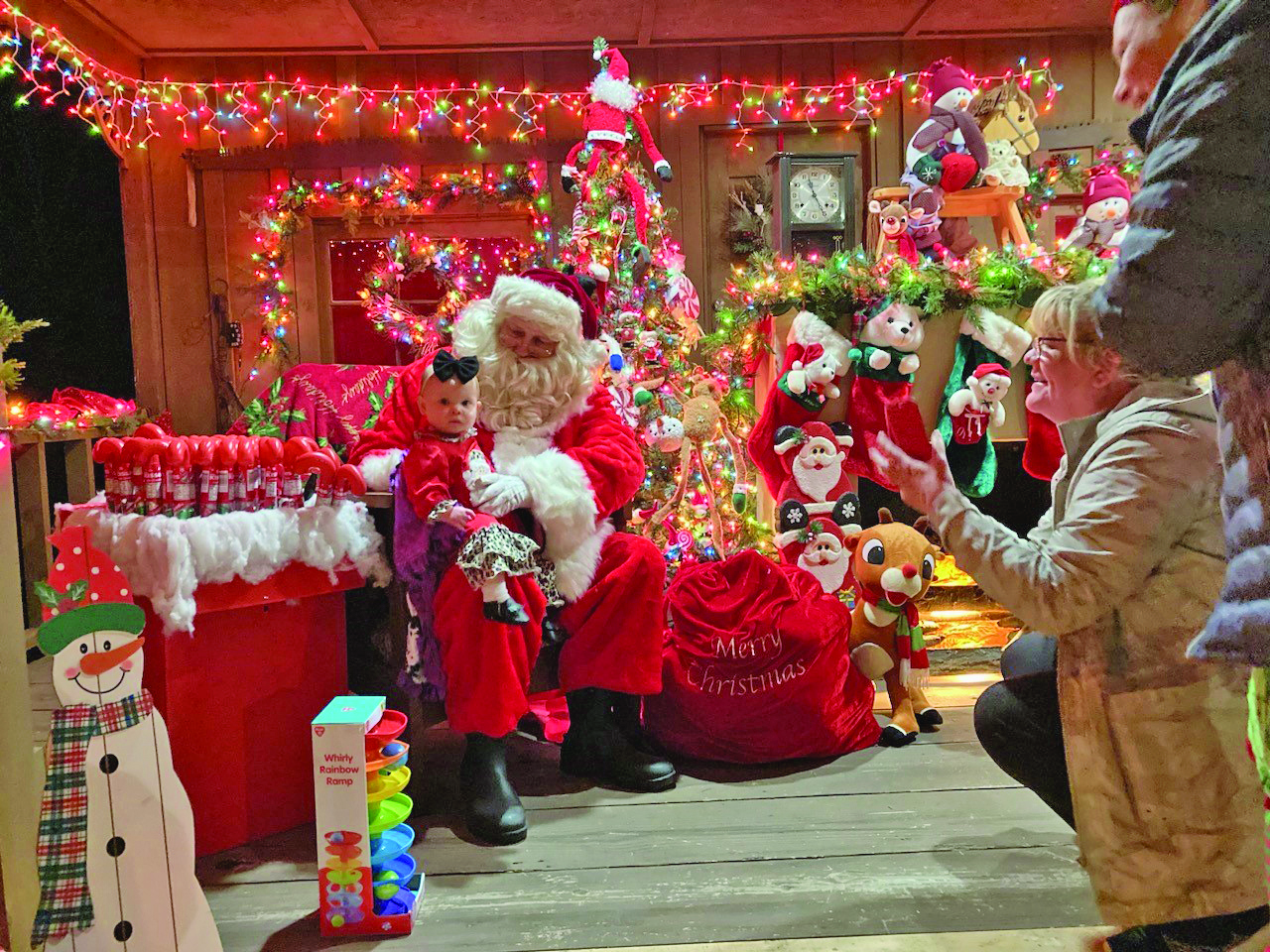 SANTA VISITS NEW EDINBURG - Jillian Luff sits on the lap of Santa Claus last Friday evening at the New Edinburg Community Center as her family tries to capture the moment with their phone cameras. The New Edinburg Community Center hosts Santa each year, providing children with free toys and treats. This year’s Santa visit was held last Friday and Saturday.