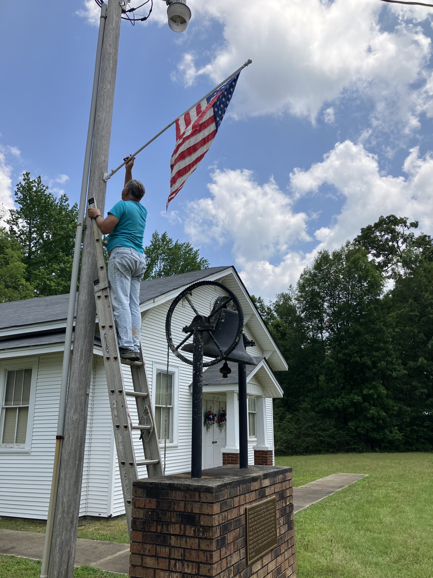 Re-New-ing Edinburg spent the week getting the town of New Edinburg ready for Memorial Day by hanging new flags. Pictured is member Roger McClellan hanging a flag at the Methodist Church above the old bell. Flags in New Edinburg will stay up through Veterans' Day in November.