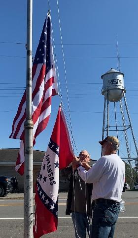 Mayor Charles Roberts and Utilities Director Joe Freyer place new United States and Arkansas flags outside City Hall. The flags were donated by Tina Thomasson Hoskins in memory of her father, R.A. (Bob) Thomasson. Bob served as the Utilities Director and Fire Chief from 1946-1971. (Photo by Connie Roberts)