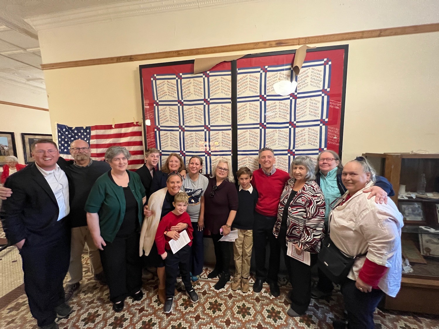 PRUETT FAMILY AT QUILT UNVEILING - Pamela Ryburn Pruett and her family gather by the Service Men's Quilt that Pruett's grandmother helped make in 1944. From left to right back row: Luke Pruett, Tim Scholes, Kim Ryburn Ferguson, Thomas Pruett, Pam Ryburn Pruett, Lauren Mitchell, Penny Ryburn Scholes, Liam Pruett, Ken Pruett, Alicia Baldwin, Sara Mitchell, Pat Ryburn. Front: April Pruett and Elliot Pruett (University of Arkansas System Division of Agriculture Photo)