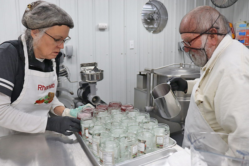 TEAMWORK — Rhonda and Ken Rudder, owners of Richland Creek Farm & Market in El Dorado, prepare their Mayhaw jelly jars at the Share Grounds processing kitchen located at the Cleveland County Farigrounds in Rison. The commercial grade kitchen can be rented by aspiring food entrepreneurs to get their product on the retail store shelf.  (Division of Agriculture photo.)
