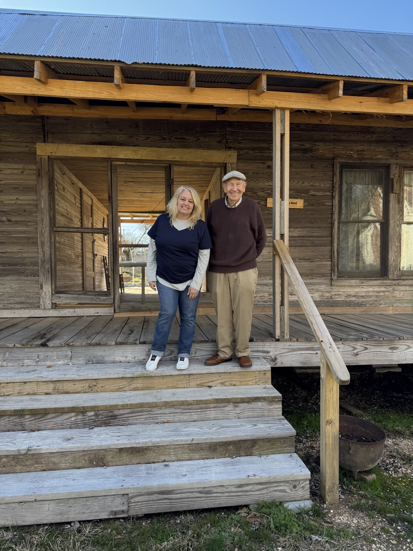 CALIFORNIAN VISITS PIONEER VILLAGE - Julie Federico of San Diego, Calif. poses with Bob Abbott on the steps of the Beard House in the Pioneer Village at Rison. (Photo by Marty Bowlin)