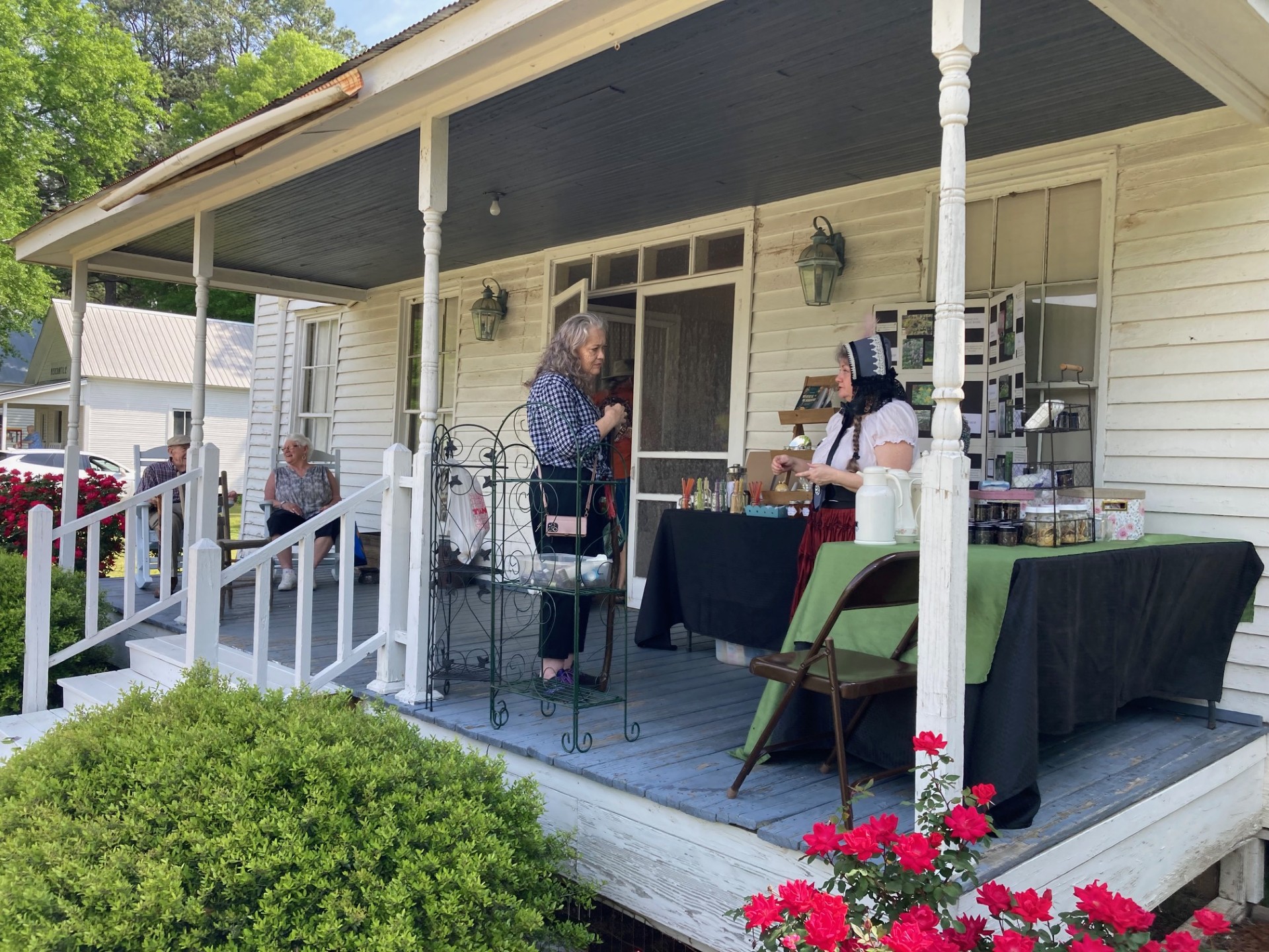 FRONT PORCH VISITING - Cindy Faulk (right) of C The Difference Boutique in Hot Springs visits with an attendee on the front porch of the McMurtrey House during the Pioneer Crafts Festival held this past Saturday. Faulk, who specializes in herbal tinctures, ointments, lotions and other products, was one of the vendors offering hand-made products at this year's festival.
