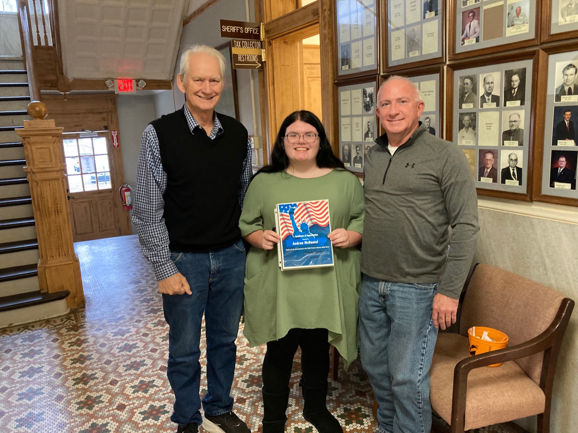Andrea McDaniel (left), a senior at Rison High School, reads the name of a candidate after selecting it from a bucket held by Cleveland County Election Coordinator Billy Bowlin (center) as Rosemary Sinclair (right), a candidate for Cleveland County Judge, looks on. The ballot draw for the March 2, 2026 primary election was held last Thursday, Nov. 4, in the hallway outside the county clerk’s office at the courthouse in Rison.