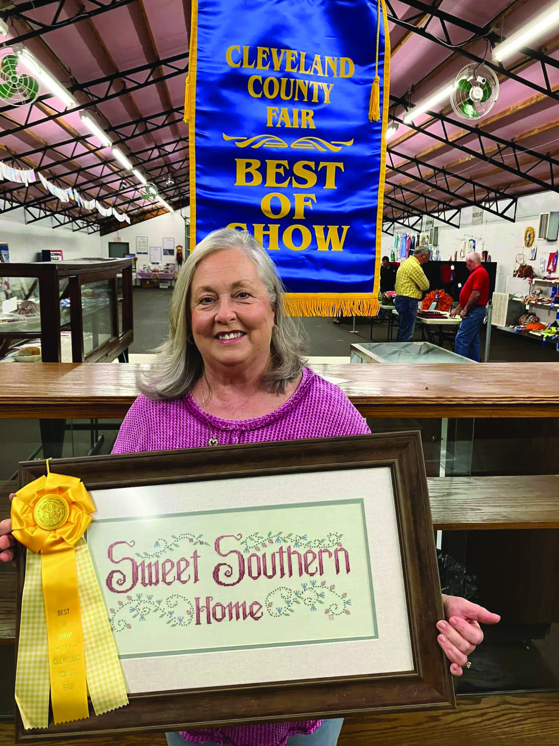 BEST OF SHOW AT THE FAIR IS A POSSIBILITY - Vickie Padgett poses with her cross stitch art which won her a Best of Show ribbon at the Cleveland County Fair in 2024. Fair President Roy Phillips and Fair Manager John Appleget explain the entry process, judging system and how points equate to ribbons and monetary prizes in this week's episode of the Free Range Conversations podcast. This year's fair is set for Sept. 16-20.