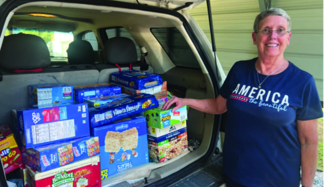 FOOD FOR STUDENTS - Donna Best, president of the Rye Extension Homemakers Club (EHC), stands next to a load of pre-packaged foods that will be going to needy students in the Woodlawn School District. The Rye EHC encourages people in the community to support this ministry that provides food for students over the weekend.