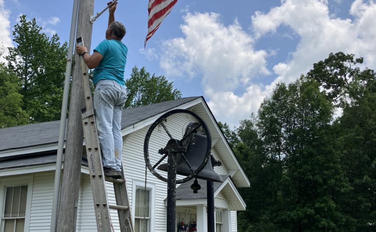 Re-New-ing Edinburg spent the week getting the town of New Edinburg ready for Memorial Day by hanging new flags. Pictured is member Roger McClellan hanging a flag at the Methodist Church above the old bell. Flags in New Edinburg will stay up through Veterans' Day in November.