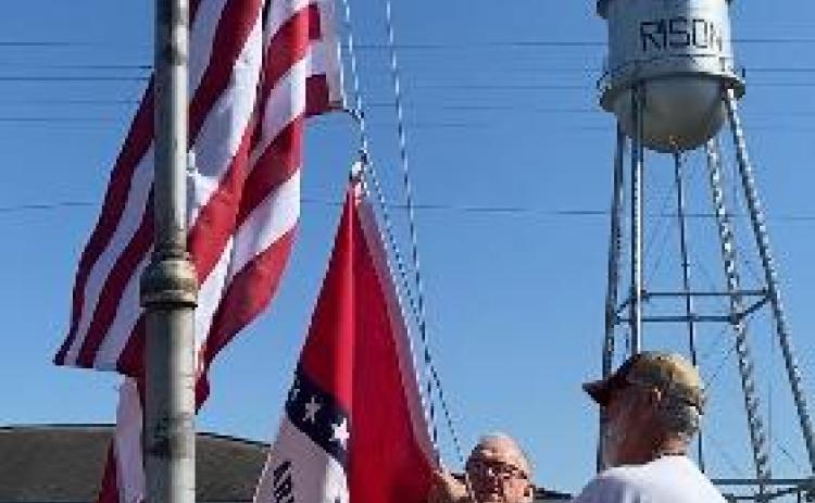 Mayor Charles Roberts and Utilities Director Joe Freyer place new United States and Arkansas flags outside City Hall. The flags were donated by Tina Thomasson Hoskins in memory of her father, R.A. (Bob) Thomasson. Bob served as the Utilities Director and Fire Chief from 1946-1971. (Photo by Connie Roberts)