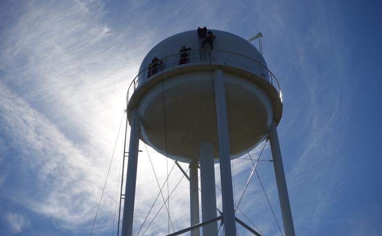 WATER TANK RENOVATION NEARLY COMPLETED - Workers on a scaffold apply the final coat of paint to the Rison water tower at Veterans Park Tuesday while another crew at the top begins to mask off the tank for a mural scene that will be painted later this week. A member of the work crew said the project could be completed by the end of the week, weather permitting. Rison was awarded at $1.62 million grant in 2023 to refurbish both of its water tanks. The “tin man” water tank next to the courthouse was completed