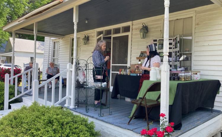 FRONT PORCH VISITING - Cindy Faulk (right) of C The Difference Boutique in Hot Springs visits with an attendee on the front porch of the McMurtrey House during the Pioneer Crafts Festival held this past Saturday. Faulk, who specializes in herbal tinctures, ointments, lotions and other products, was one of the vendors offering hand-made products at this year's festival.